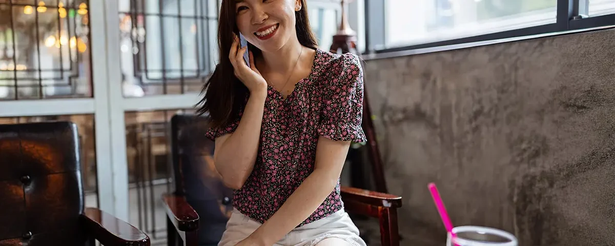 A happy woman talking on her smartphone while sitting in a bright restaurant, illustrating the excitement of dating and communication.