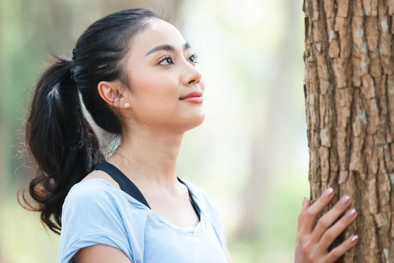 Filipina with thoughtful expression embracing tree in forest
