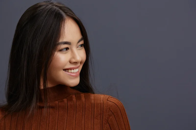 Woman smiling confidently in casual brown sweater against neutral background