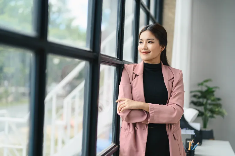 Confident professional woman in modern office setting wearing pink blazer