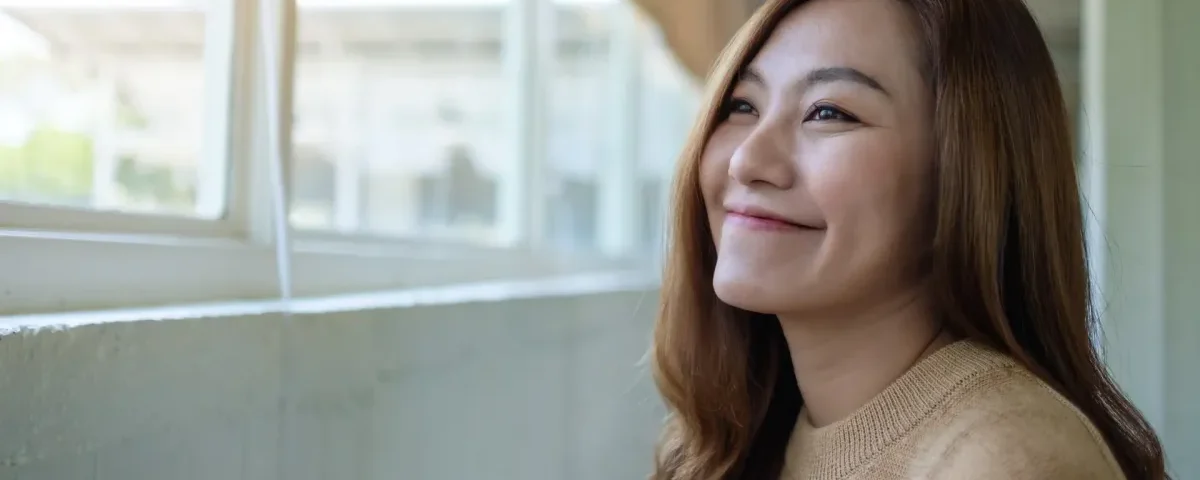 Serene Asian woman gazing peacefully toward a window in soft indoor light