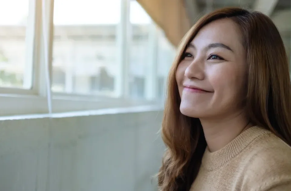 Serene Asian woman gazing peacefully toward a window in soft indoor light