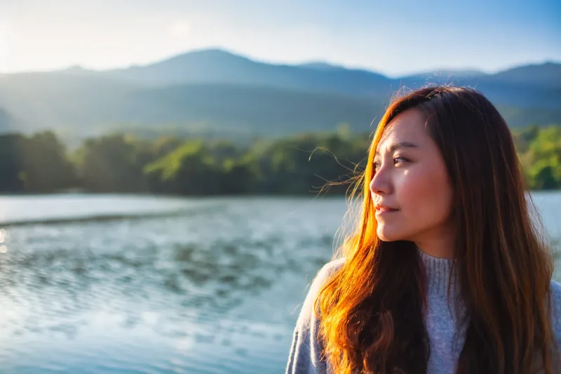 Contemplative Asian woman at golden hour in natural landscape setting