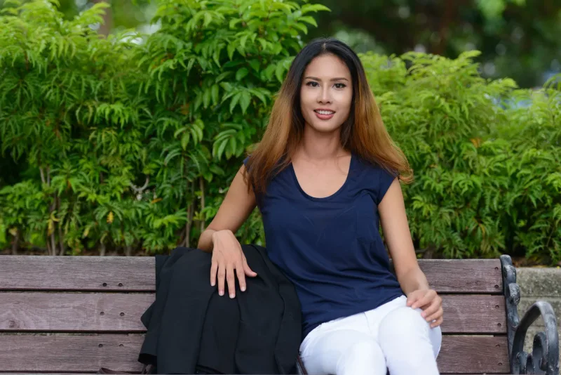 Joyful Asian woman seated outdoors in garden setting with warm smile