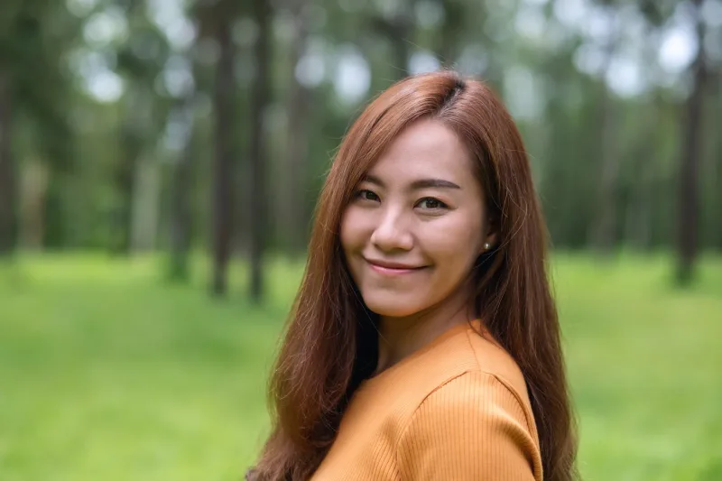 Smiling Asian woman in natural outdoor setting amid greenery