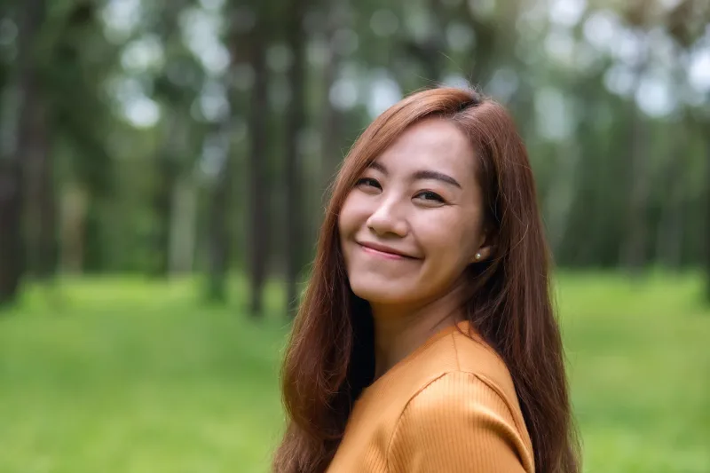 Relaxed young woman smiling outdoors in natural garden setting