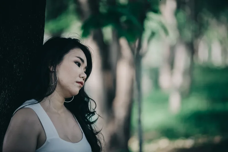 Woman in thoughtful pose by tree, reflecting the patience and emotional presence required for genuine Asian dating connections.