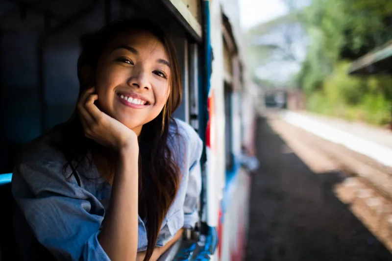 Woman smiling by train window, capturing the genuine joy and presence that authentic connection-building creates.
