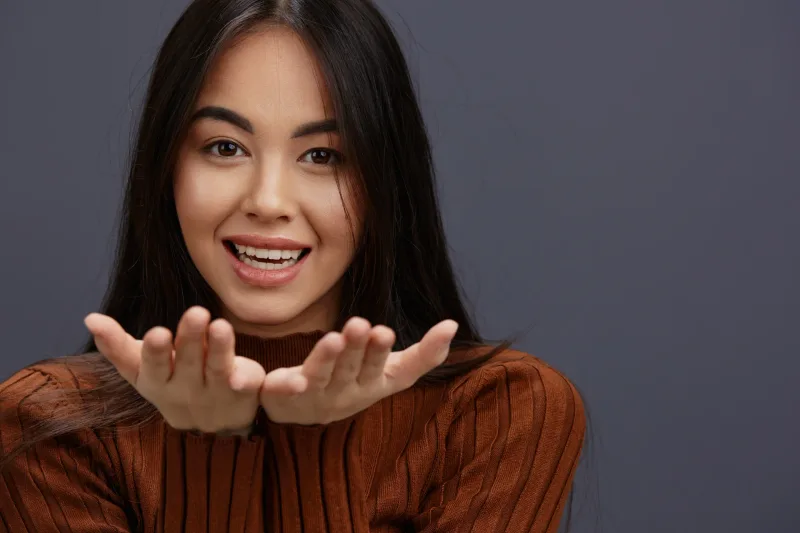 Woman in brown sweater with joyful, welcoming expression and open gesture
