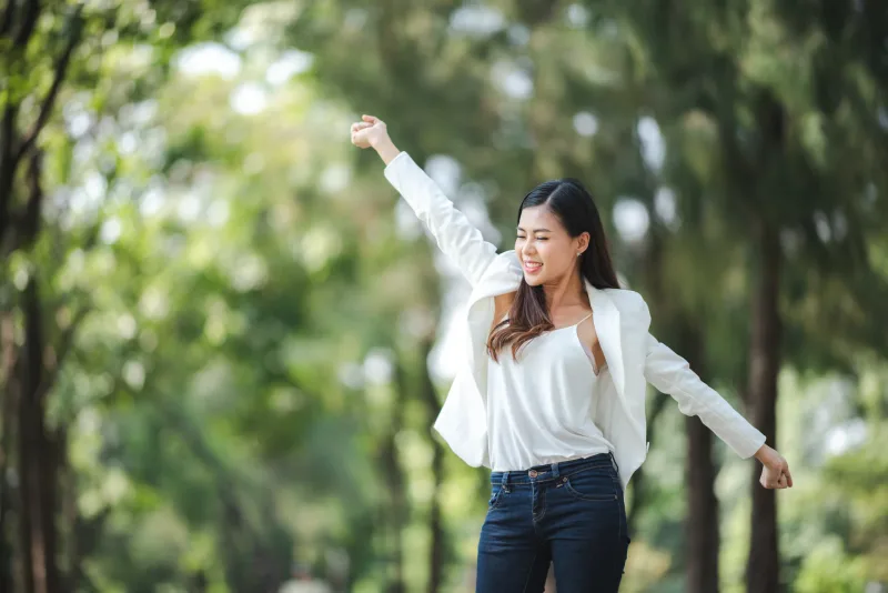 Woman with arms raised in park celebrating, showing genuine joy and enthusiasm in outdoor setting
