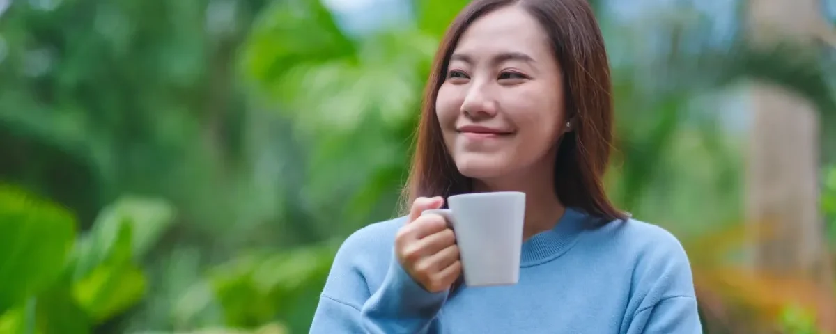 Woman enjoying coffee outdoors with serene expression