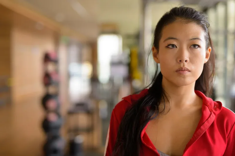 Thoughtful Asian woman in red jacket with focused contemplative gaze