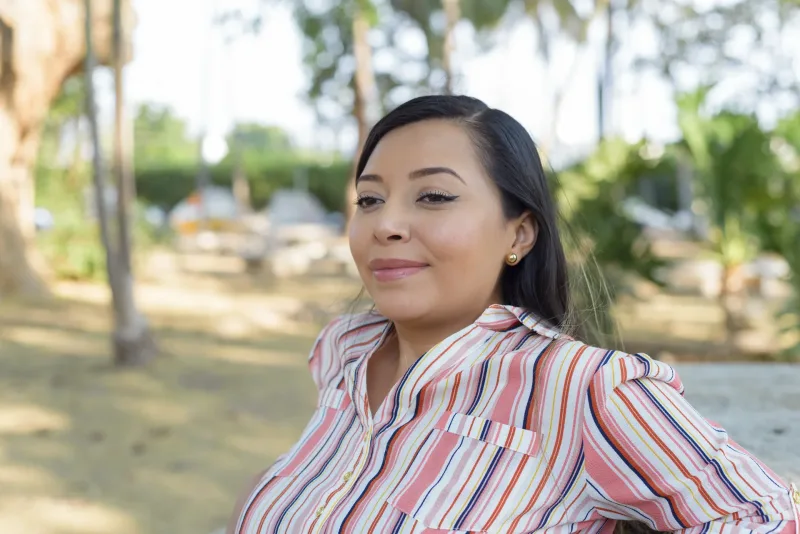 Woman in striped shirt sitting pensively on park bench, contemplative expression