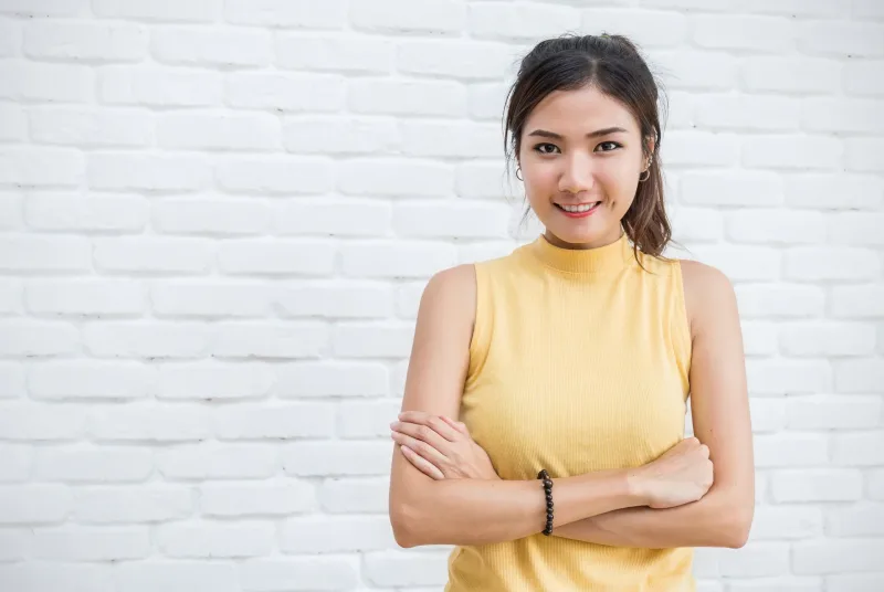 Woman in yellow top posing against brick wall, confident expression