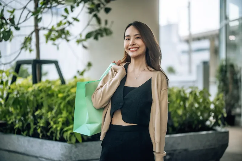 Woman smiling with shopping bags in an outdoor urban garden setting