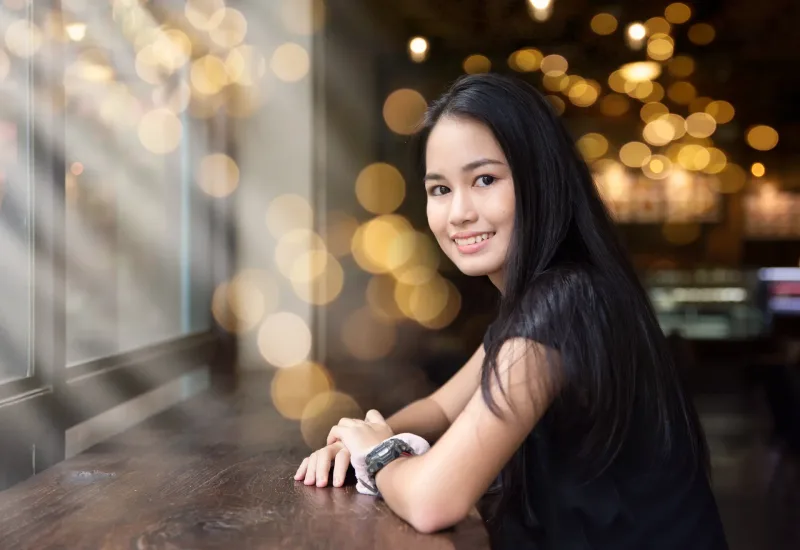 Woman at cafe table with evening bokeh lights, relaxed and present