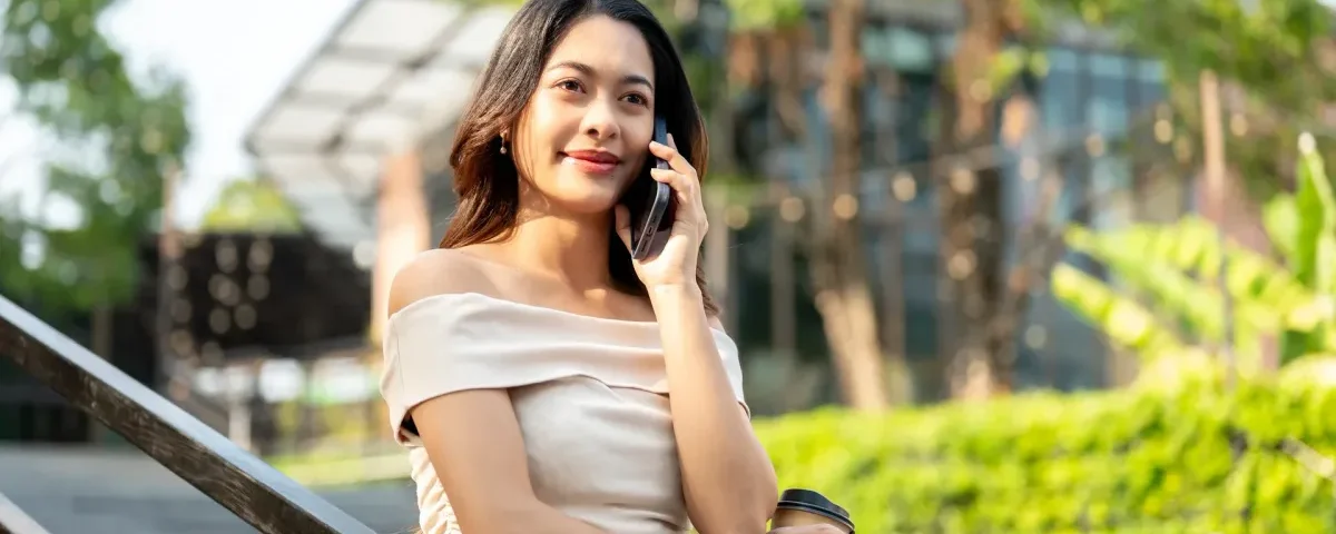 Woman holding coffee with relaxed confidence during outdoor phone conversation