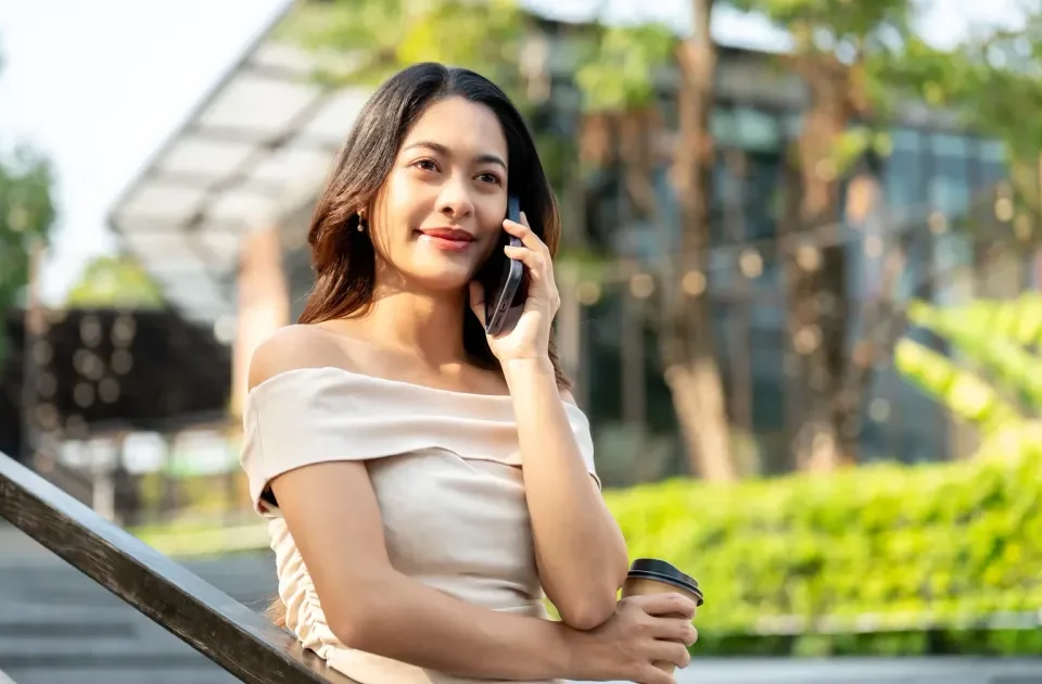 Woman holding coffee with relaxed confidence during outdoor phone conversation