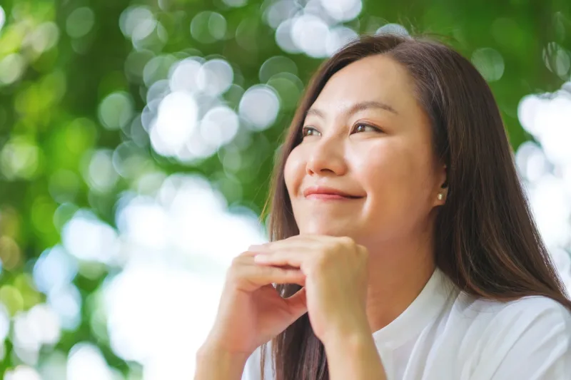 Thoughtful woman relaxing outdoors with peaceful expression and soft bokeh background
