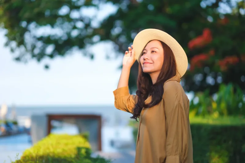 Woman smiling in garden with straw hat, demonstrating genuine warmth