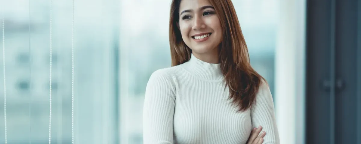 Woman in turtleneck smiling confidently near window