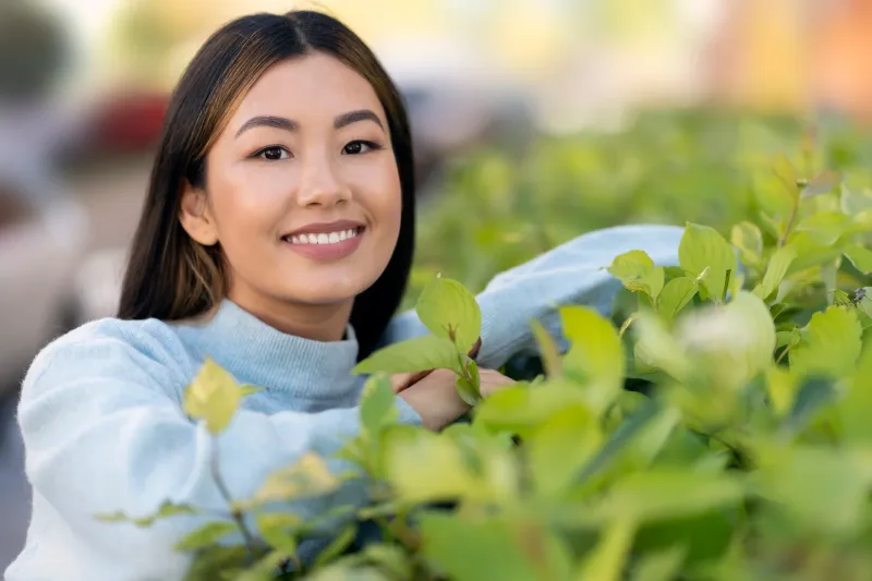 Woman smiling outdoors surrounded by green plants
