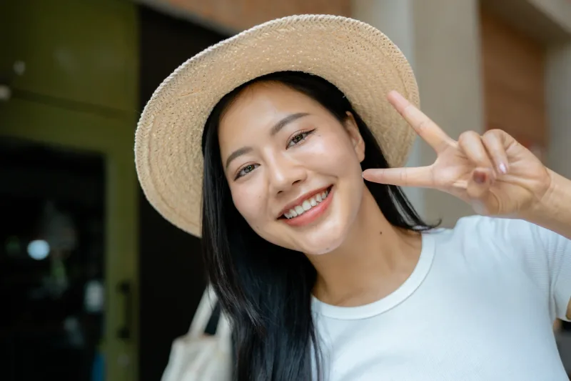 Woman in straw hat making peace sign with joyful expression