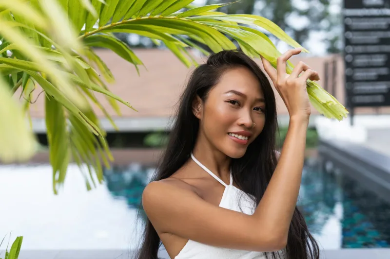 Woman smiling near poolside in tropical setting with palm fronds