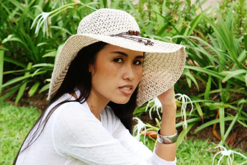 Woman in straw hat at park with thoughtful expression, garden background