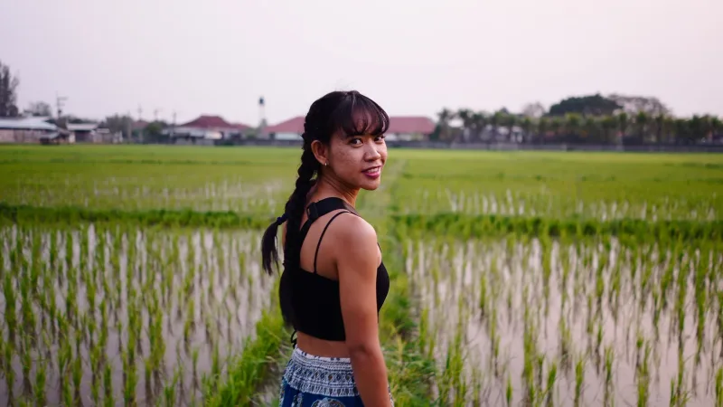 Woman in rice field looking back over shoulder, contemplative expression
