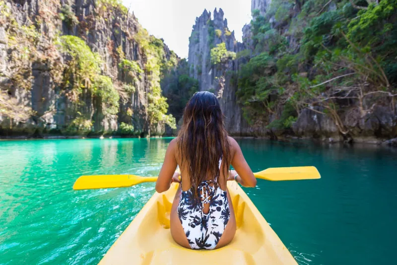 Woman kayaking in tropical lagoon with turquoise water and scenic cliffs