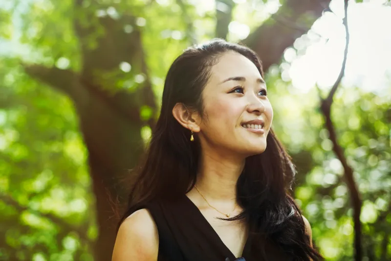 Woman smiling peacefully in natural forest setting amid greenery