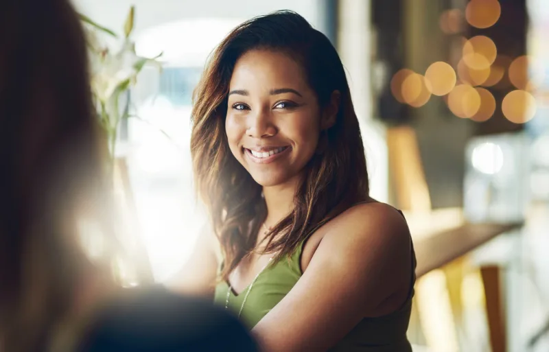 Woman smiling warmly in café setting, representing genuine engagement and comfort in conversation