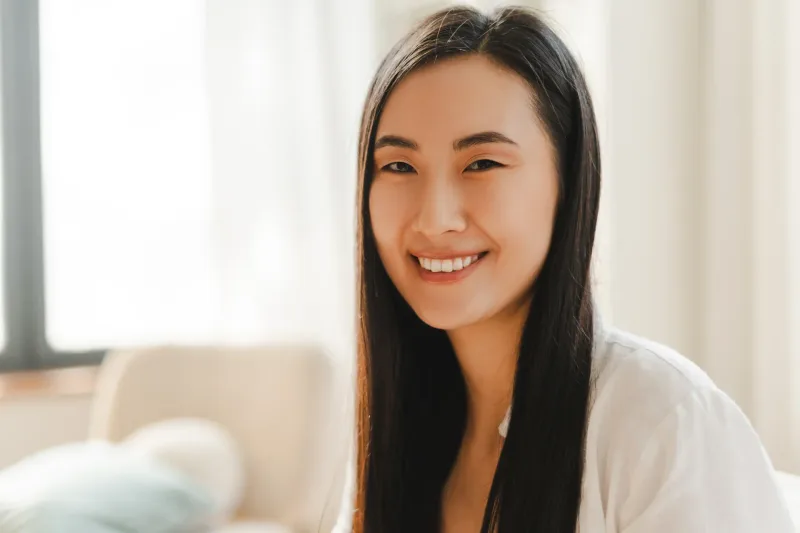 Woman with long black hair smiling indoors with warm natural lighting