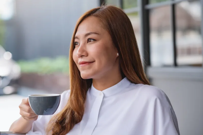 Woman holding coffee indoors with relaxed, contemplative composure