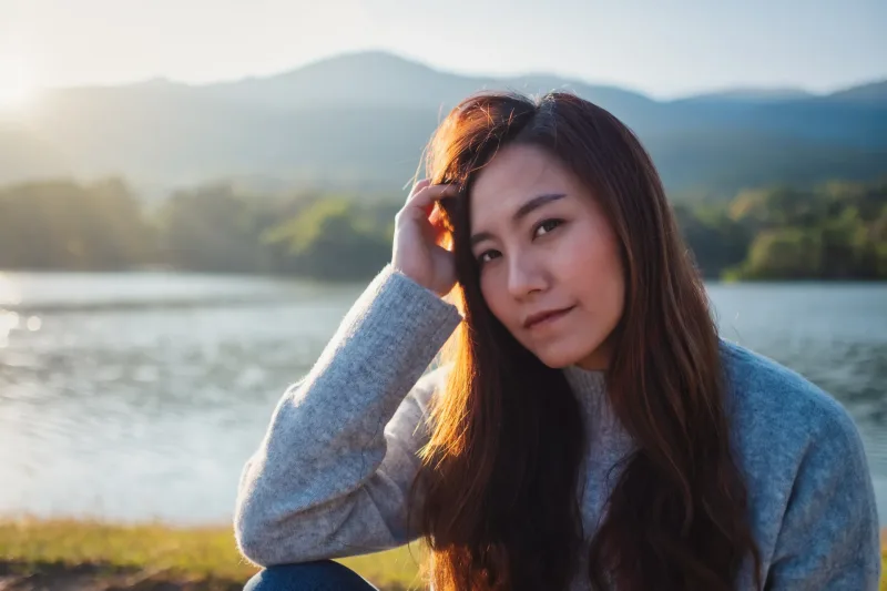 Asian woman with serene expression at lakeside during golden hour
