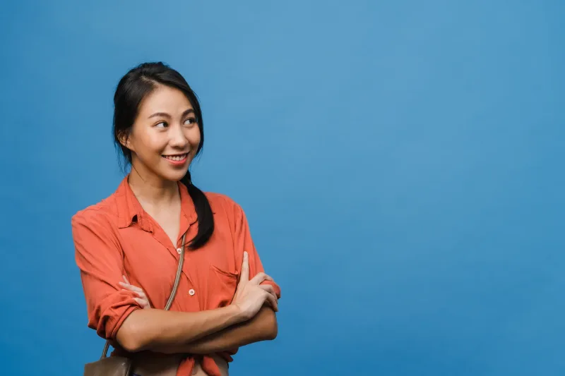 Woman in orange shirt smiling in studio setting, embodying confidence and friendly demeanor.