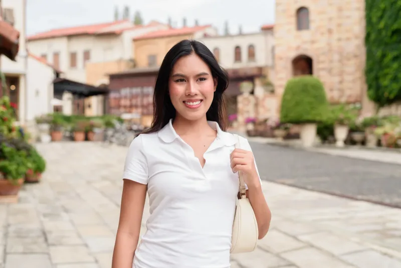 Asian woman walking outdoors in casual style against European architecture, suggesting arrival and travel.