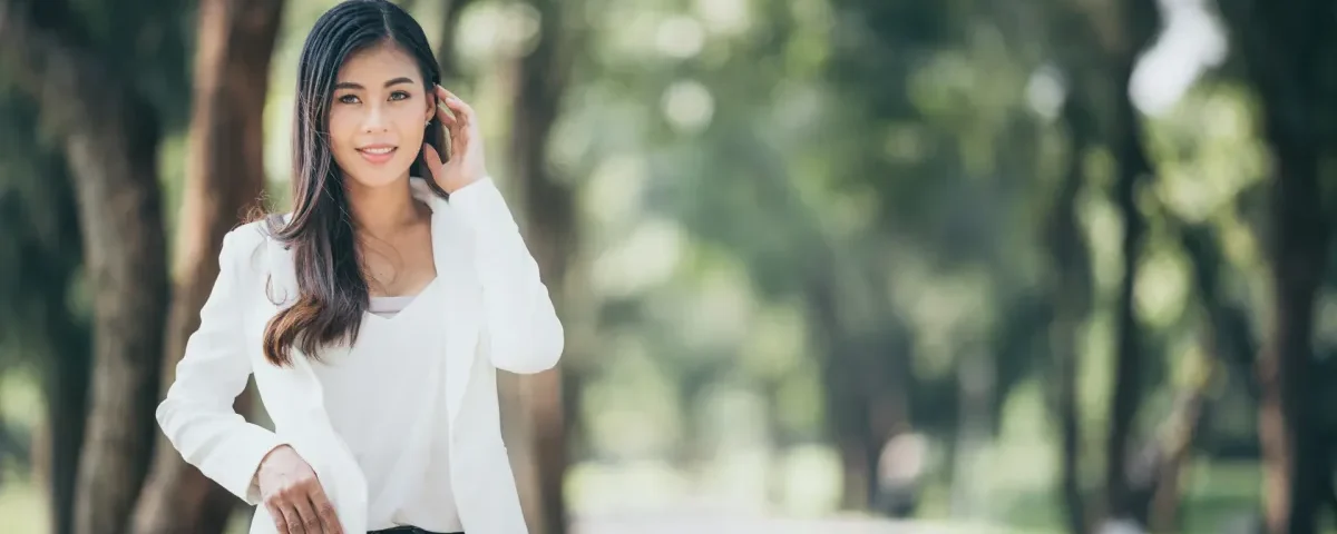 Woman in elegant white blazer posing confidently in a green park setting