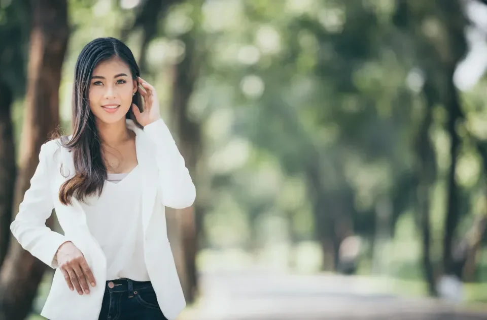 Woman in elegant white blazer posing confidently in a green park setting