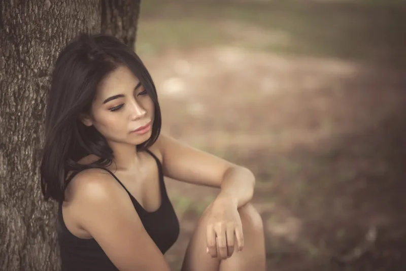 Woman sitting outdoors in contemplative thought by tree