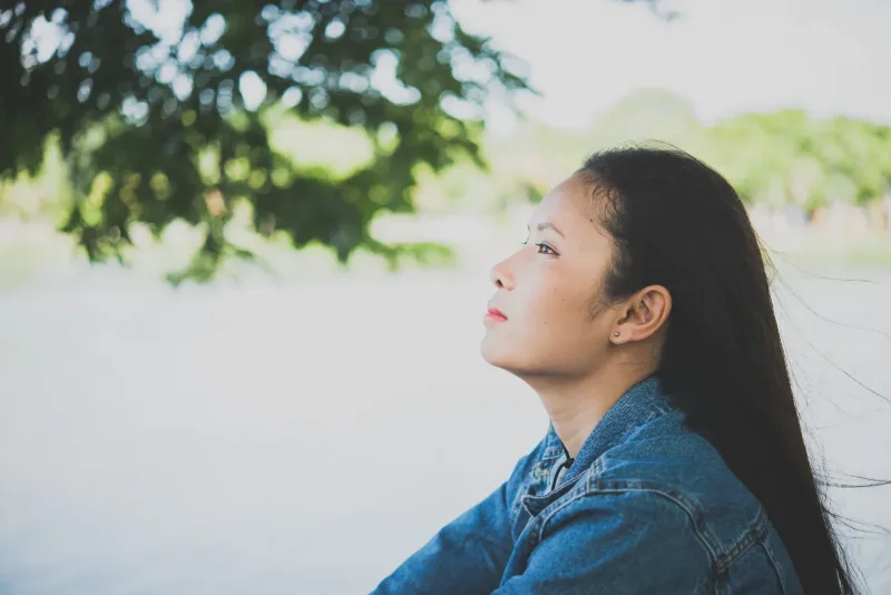 Woman in denim jacket gazing thoughtfully at park