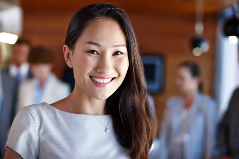 Professional woman smiling in modern office setting with window background.
