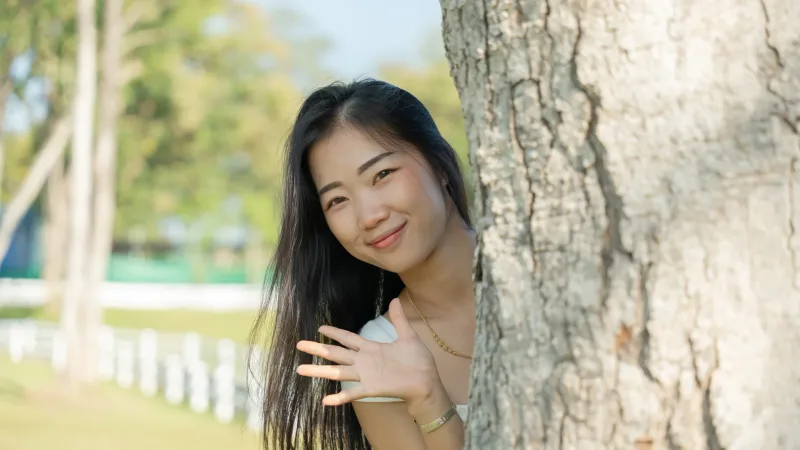 Woman smiling outdoors near tree with smartphone and gentle pose