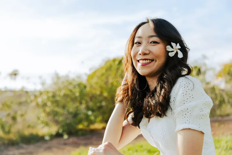 Filipina sitting in a field with white flower accessory, radiating joy and belonging