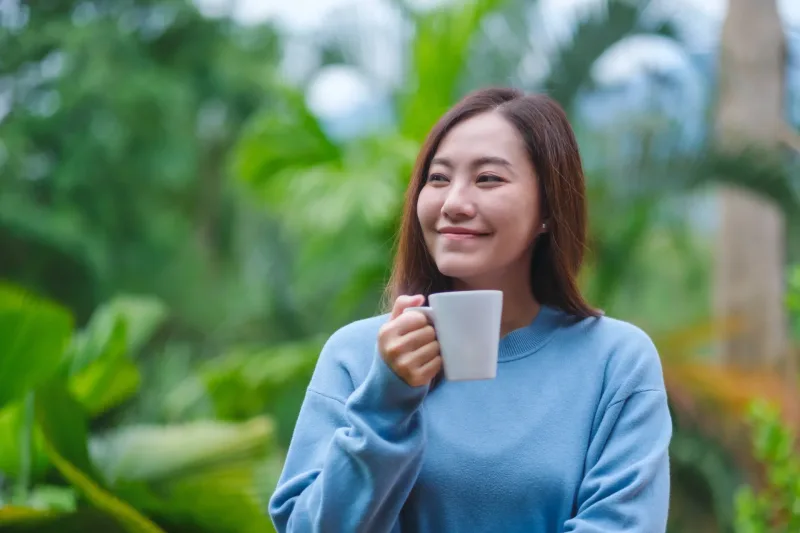 Woman relaxing with coffee outdoors in peaceful setting, illustrating the balance between economic context and genuine human connection in Philippines dating